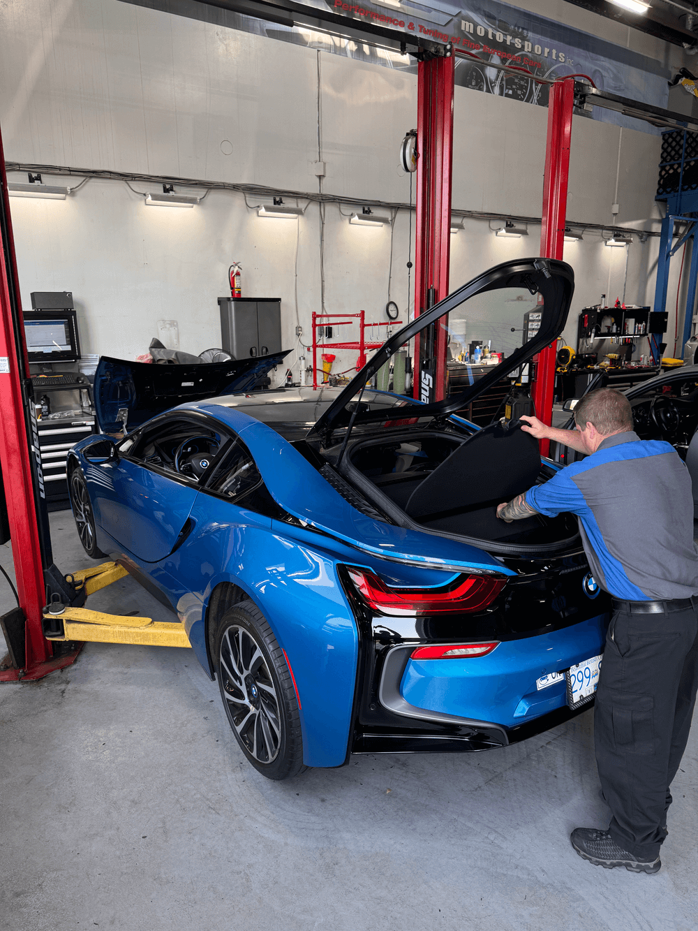 BMW EV technician examining a blue BMW i8 at CG Motorsports